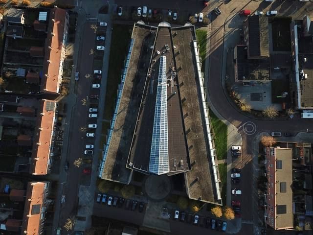 Droneshot van een lang gebouw met centrale lichtstraat over de volledige daklengte, stedelijke omgeving