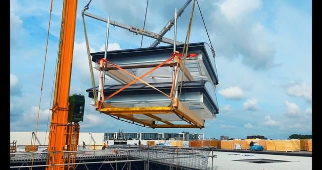 Kraan hijst prefab gebogen lichtstraatunit boven industrieel dak, NS treinstelhallen