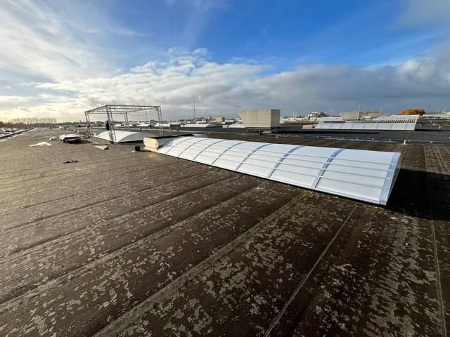 Groot plat industriedak met een rij langwerpige lichtstraten die in de verte verdwijnen, dramatisch zijlicht