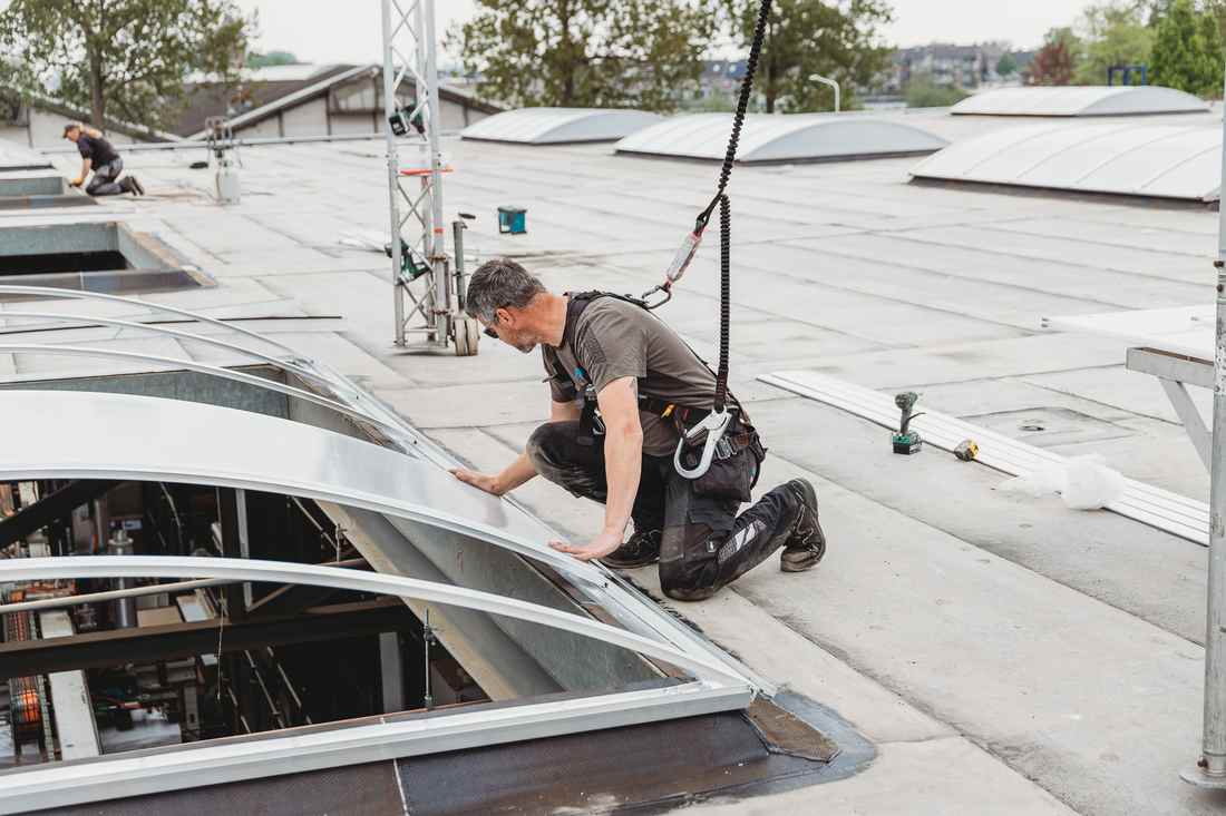 Twee monteurs van Hakvoort Daglicht installeren gebogen lichtstraten op een bedrijfsdak