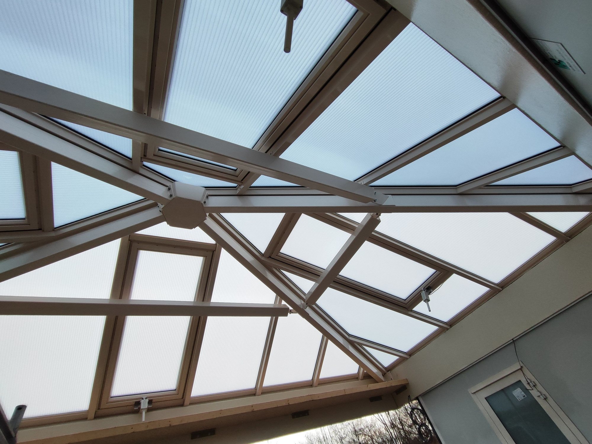 Interieur van een glazen piramidedak met houten draagconstructie, delen geopend voor ventilatie