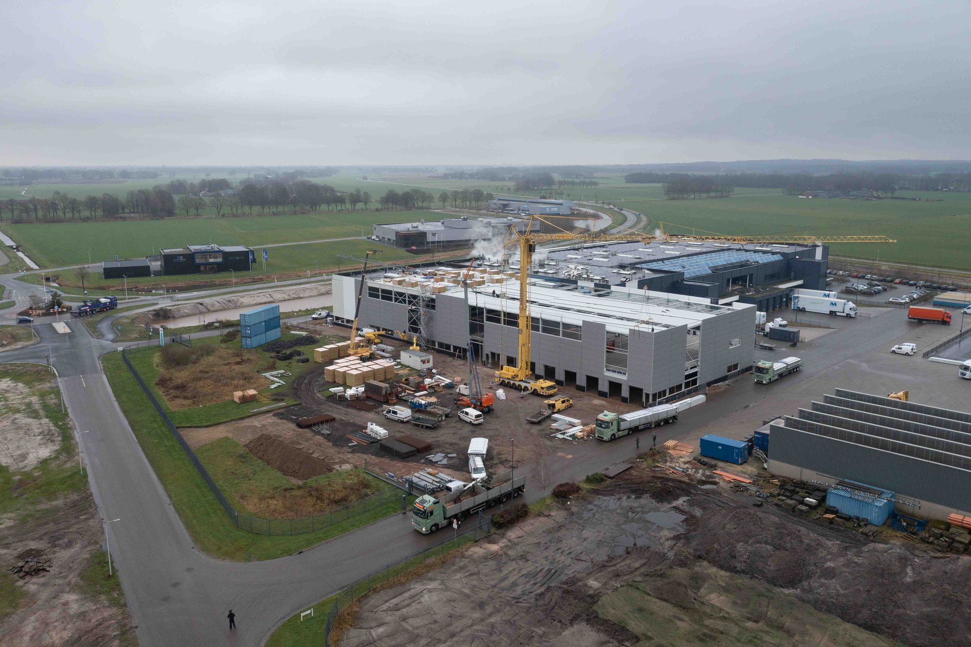 Luchtfoto van een bedrijfsdak tijdens de aanleg van meerdere lichtstraten, bouwkraan naast het complex