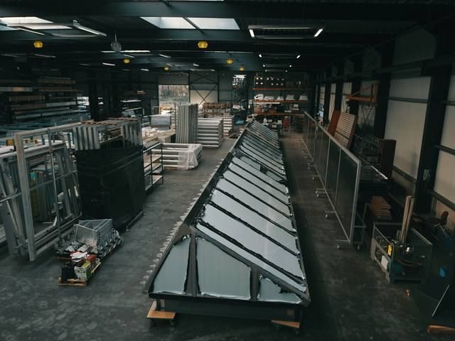 Prefab sheddak-element diagonaal op de voorgrond in de productiehal, rijen elementen erachter