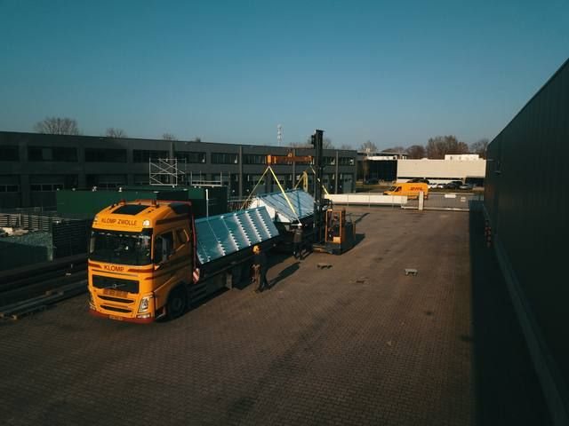 Gele autolaadkraan geladen met prefab sheddak-elementen in laag ochtendlicht